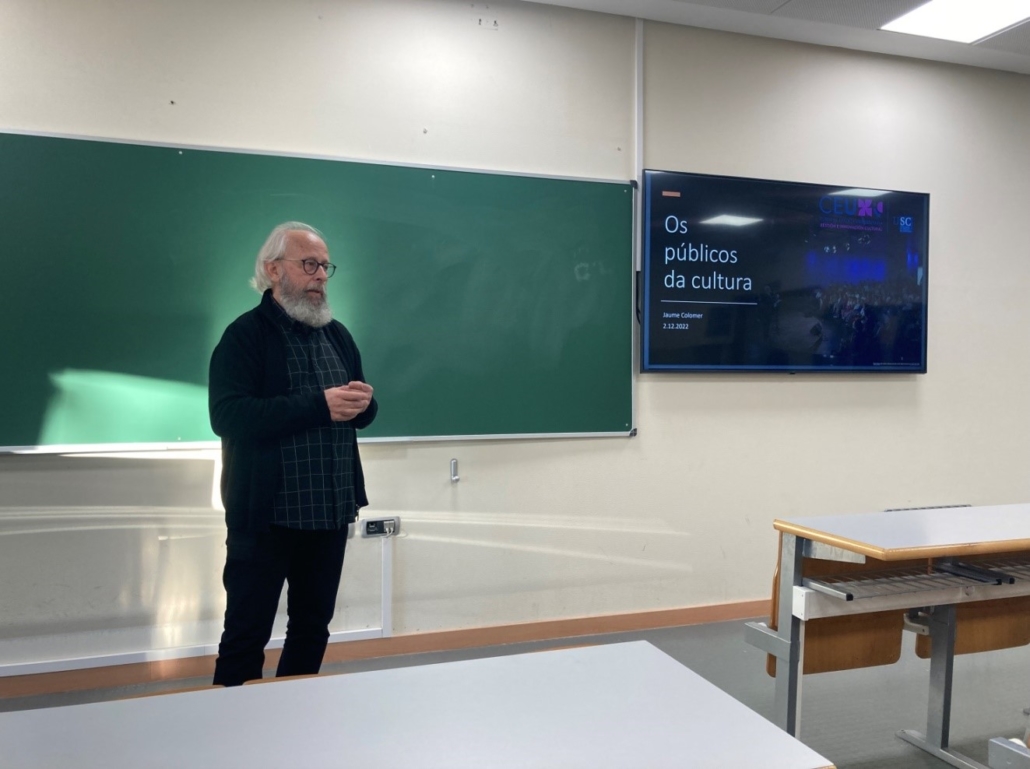 Jaume Colomer, no comezo da sesión, de pé diante da pizarra. Á súa dereita, a pantalla na que se proxecta a súa presentación, que leva por título "Os públicos da cultura"
